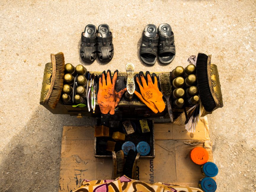Aerial view of a shoe shine setup with brushes, polish, gloves, and sandals on a concrete surface.