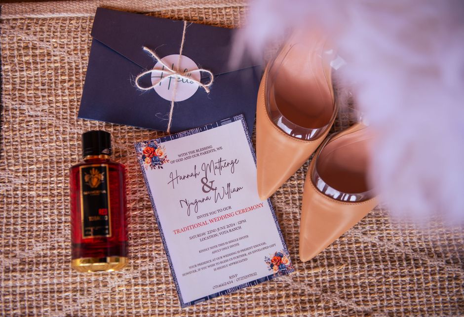 Stylish flat lay of wedding invitation, heels, envelope, and perfume bottle on textured surface.