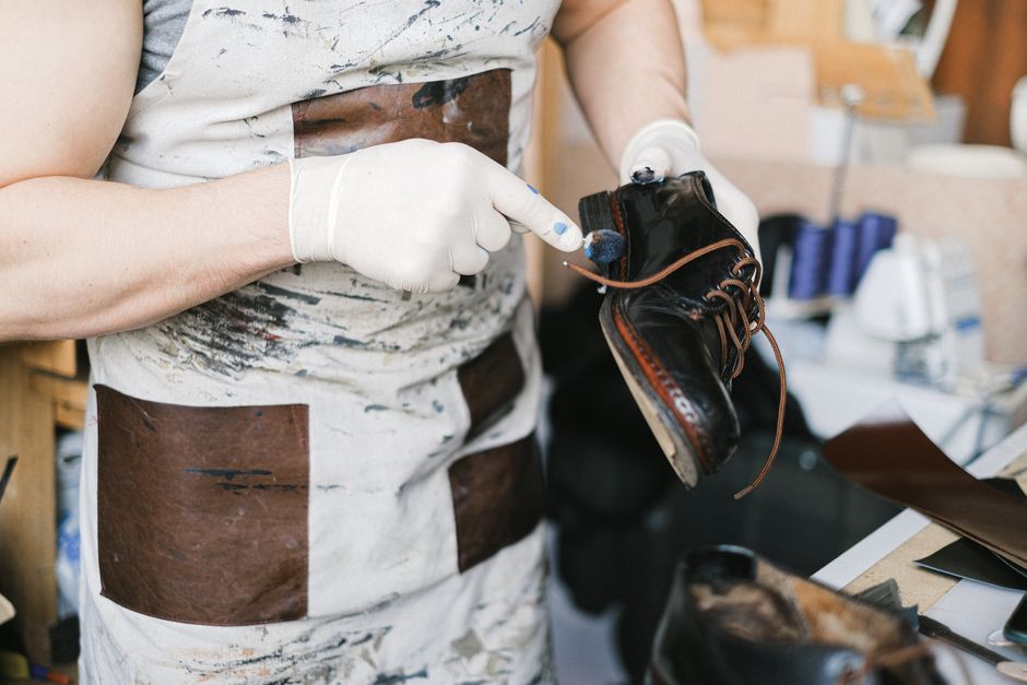 A craftsman polishing black leather shoes with gloves in a workshop setting.